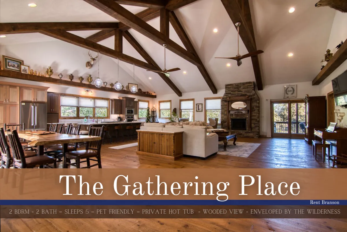 A spacious great room featuring a large stone fireplace, exposed wooden beams on a vaulted ceiling, and a generous seating area. Expansive windows along one wall showcase tranquil wooded views and allow abundant natural light to fill the space, embodying the heart of the home for gatherings and relaxation.
