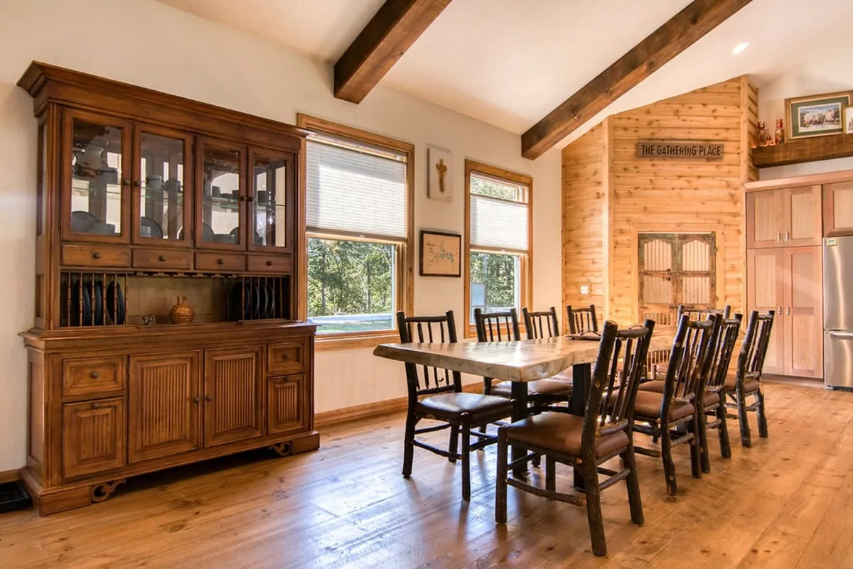 A welcoming dining area with a large table and hutch, framed by windows that look out onto tranquil woodlands. The warm decor and ample seating set the scene for shared meals and festive gatherings.